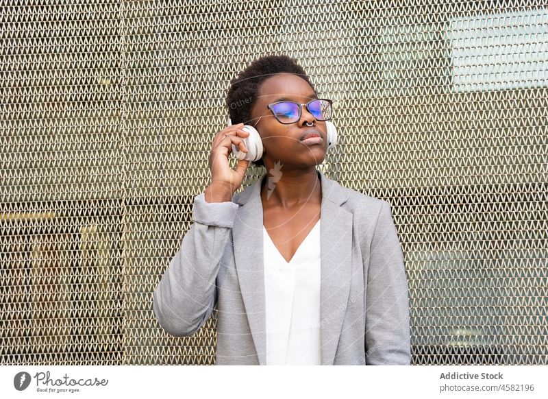 Young African American woman listening to music in headphones grid song fence wireless gadget device street positive sound melody meloman audio confident