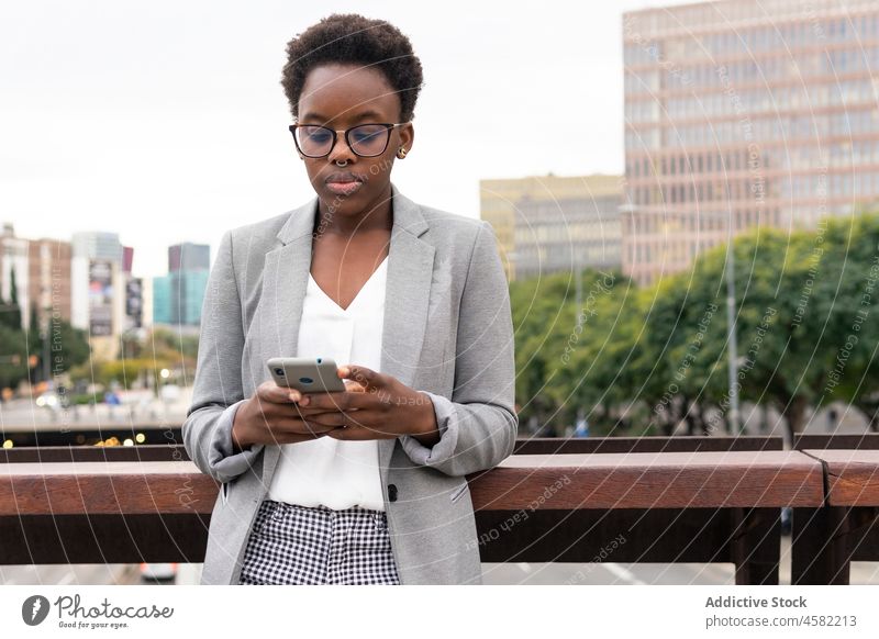 Young African American woman using smartphone on balcony browsing cellphone businesswoman worker formal employee surfing executive city career professional