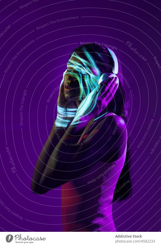 Brazilian woman in headphones with shadow of light on face style trendy fluorescent portrait projector neon cool music song illuminate dark eyes closed reflect
