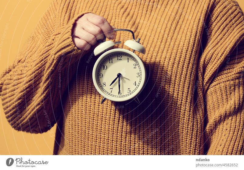 round alarm clock in a woman's hand, the time is half past seven in the morning. Woman in orange sweater alert analog arrow awake background bell business