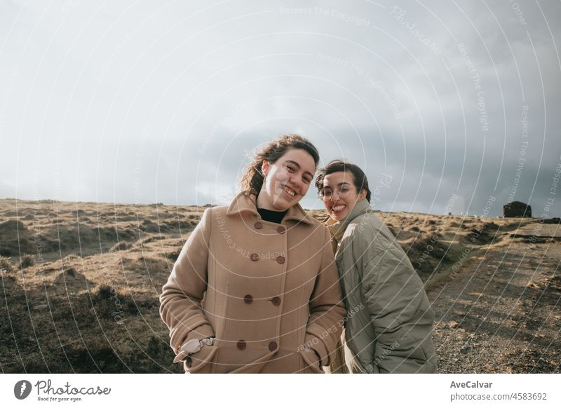 Two young women, on winter cloths during a windy day, enjoying a day while having fun running togueter between electric windmill . Lifestyle. Hipster and modern style. Cinema style.