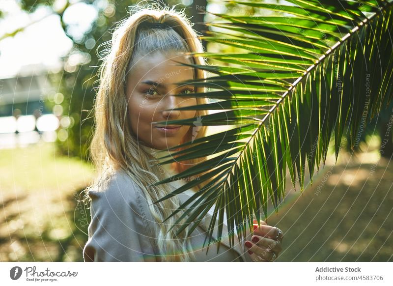 Young woman near green palm leaf in sunny day park portrait tree charming tropical nature blond relax garden rest carefree natural idyllic tranquil calm foliage