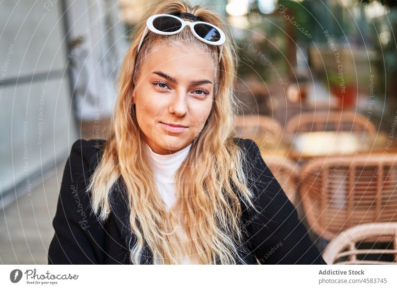 Positive woman sitting at table in terrace of cafe veranda portrait relax trendy blond positive chill jacket content sunglasses cafeteria casual pleasant