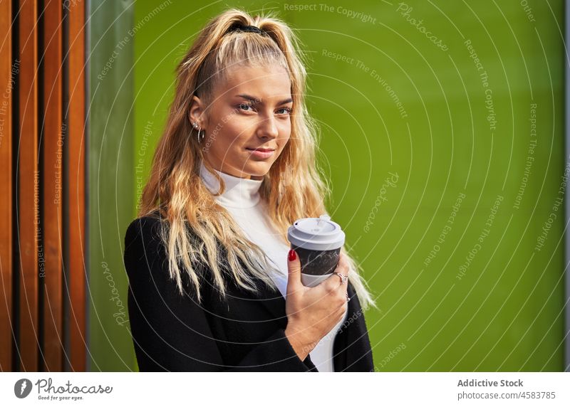 Young blonde woman with takeaway coffee and backpack style dream rest leather urban beverage dreamy coat wooden calm wall paper cup break smile hot drink