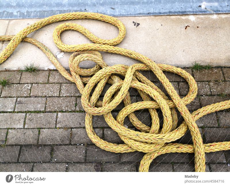 Yellow shimmering ship's rope on grey paving stone at a landing stage in the harbour of Norddeich near Norden in East Frisia in Lower Saxony Rope Dew
