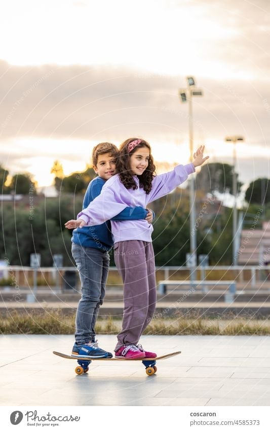 Two kids riding together wtih a skate board active activity balance boy child childhood children enjoy enjoying family friends fun game girl happy healthy learn