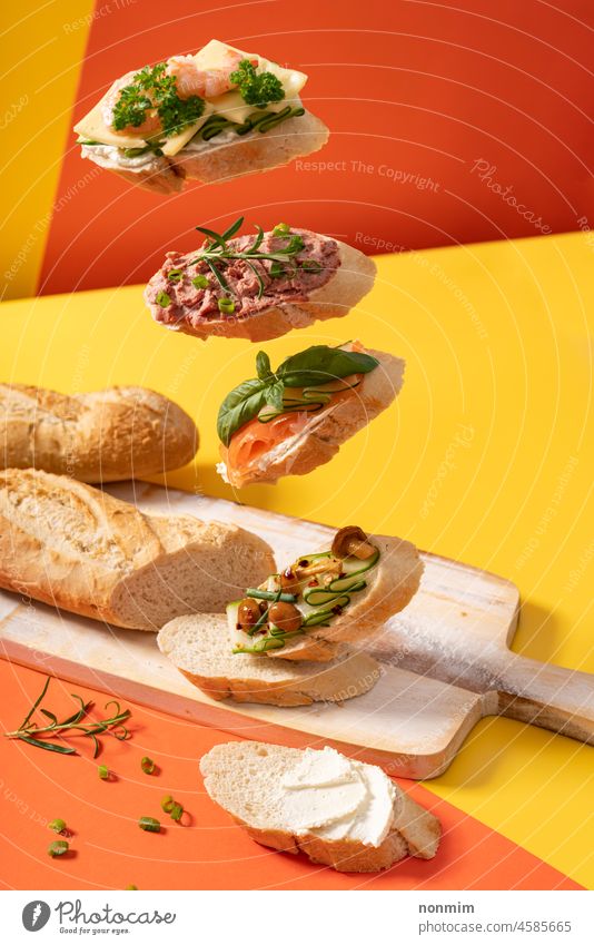 Little levitating baguette sandwiches on vibrant yellow and orange background decorated with greens Baguette green leaves herbs appetizer snack bread breakfast