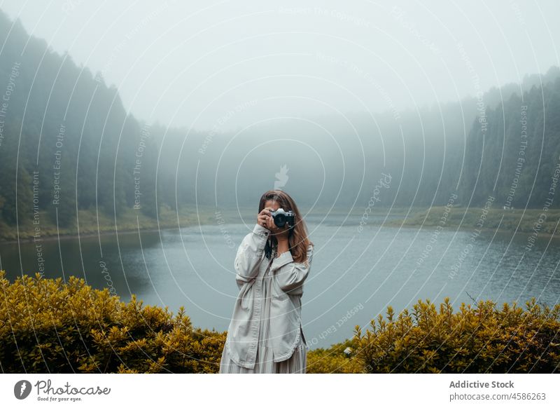 Anonymous woman standing near lake with camera forest nature fog photographer photo camera take photo travel vacation female traveler using azores sao miguel