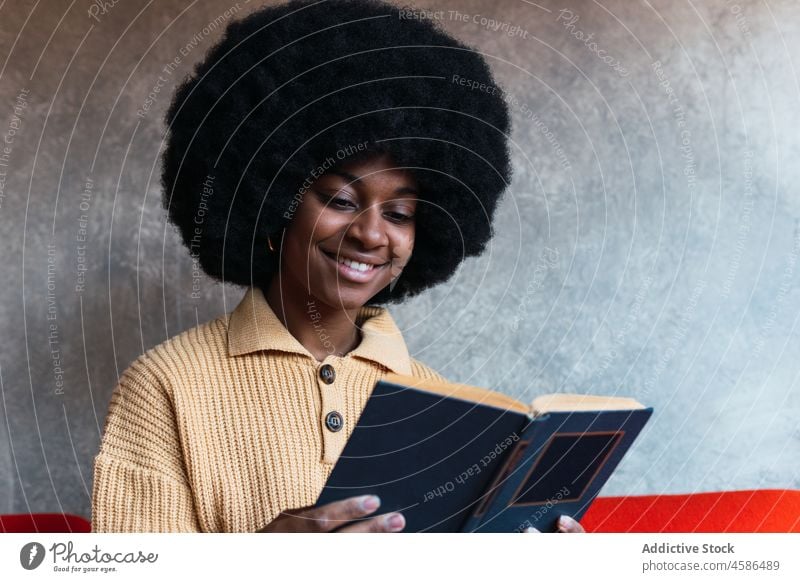 Smiling black woman reading book on sofa couch home literature free time comfort relax female african american afro attentive hobby young concentrate novel rest