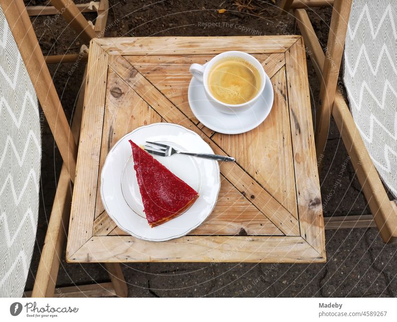 Fresh coffee and a piece of fruit cake with red fruits on a small wooden table in front of a café in the summer in the north end of Frankfurt man Main in Hesse
