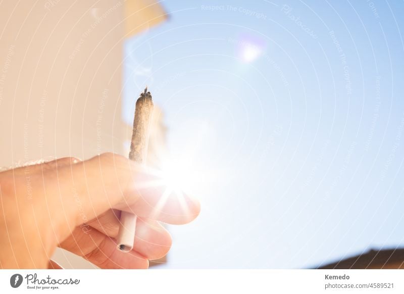 Hand with a marijuana joint with the sky and sun in the background. cannabis weed cigarette copy space backdrop sunny outdoor banner horizontal smoke pot nature