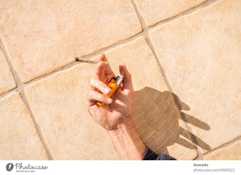 Person lying in the sun holding a marijuana joint and a lighter. Background of person relaxing and smoking in the sun. cannabis weed cigarette copy space