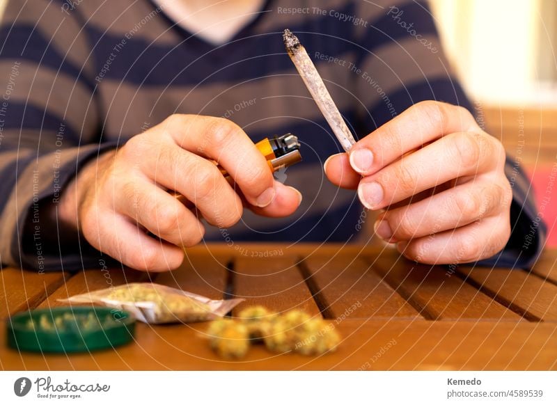 Front view of young person smoking cannabis joint on a table full of weed. man smoke marijuana pot adult light lighter millennial street friends lit puff sit