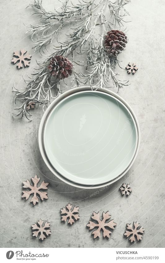 Winter table setting with empty plate, fir branches , decoration snowflakes and pine cones on pale grey table. Top view with copy space. Frame winter top view