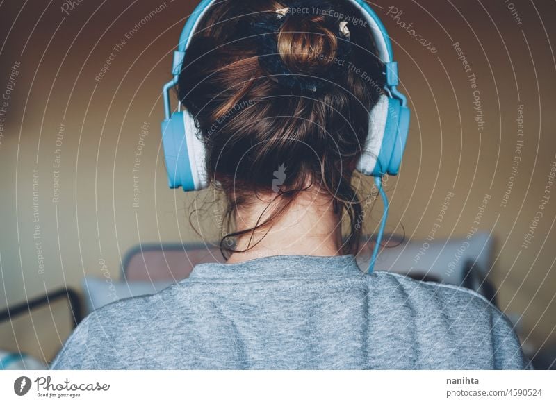 Young woman listening to music and wearing cozy clothes headphones headset young youth teen back view bun hair hairstyle comfort home casual candid technology