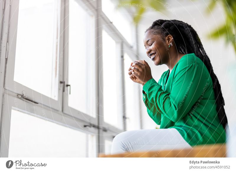 Young woman with cup of coffee looking out of window black millennials hipster indoors loft natural adult one attractive successful people confident person