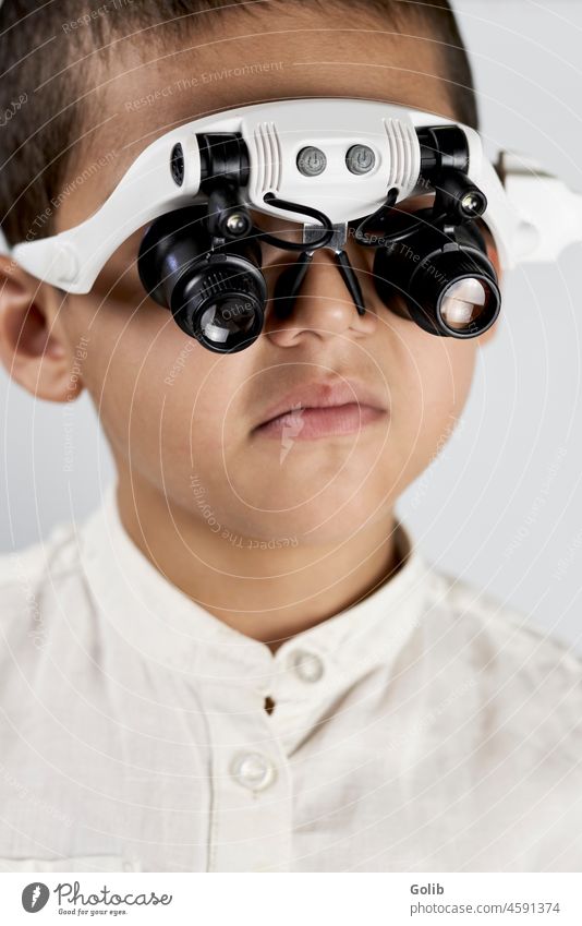 A schoolboy in special eyeglasses little scientist magnifying back to school looking at camera close-up handsome kid headset studio detective searching evidence