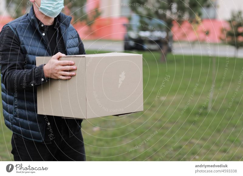 Delivery man in red cap, face medical mask hold empty cardboard box outdoors. Service coronavirus. Online shopping. mock up. hand guy covid-19 2019-ncov