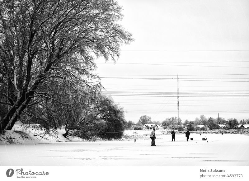 winter fishermen on ice and snow covered river under electric transmission lines, black and white activity beautiful beginning of winter christmas cold