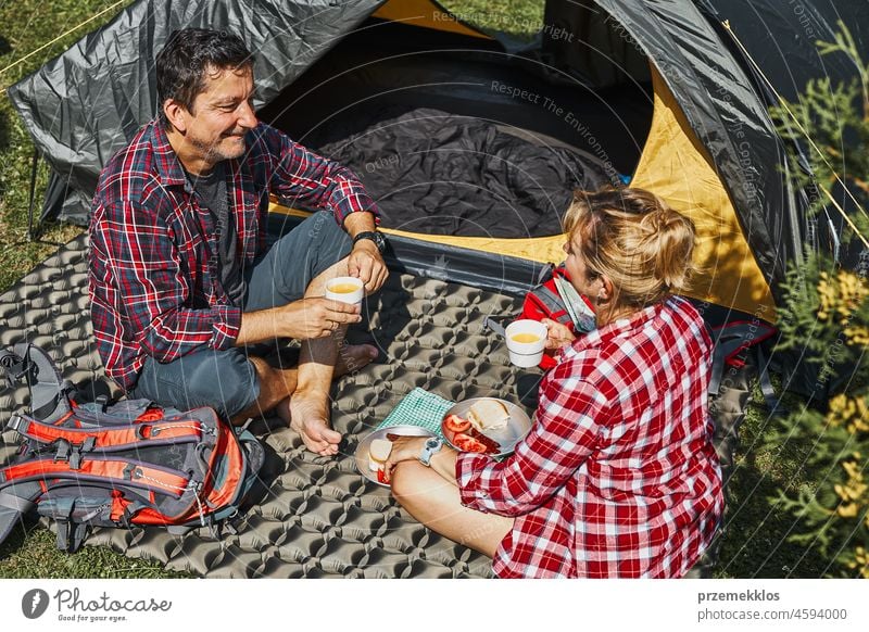 Couple having breakfast sitting by tent at camping. People actively spending summer vacations close to nature outdoors trip adventure campsite traveling couple