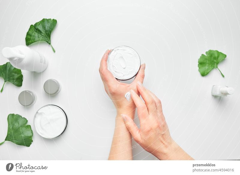 Woman applying  cosmetic moisturizing hand cream. Cosmetic products, green leaves on white table. Spa, manicure, skin care concept nail woman beauty moisturizer