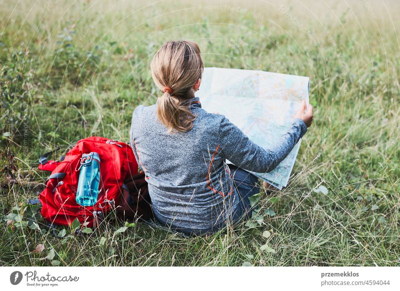 Woman with backpack having break during trip in mountains looking at map sitting on grass summer active woman adventure activity fun travel trekking vacation