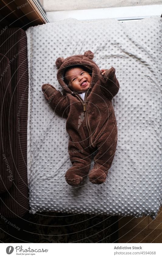Smiling ethnic baby in soft bear overall on blanket newborn joy laugh funny playful happy expressive adorable lying babyhood infant little childhood plaid