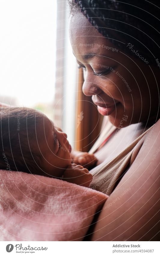 African American woman kissing newborn baby on hands child tender mother care love window home hug parent comfort embrace towel bonding apartment wrap