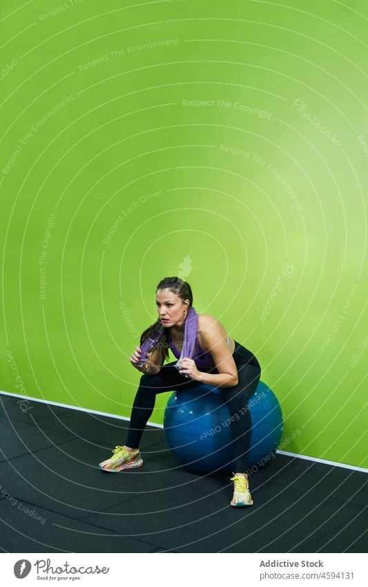 Ethnic sportswoman sitting on fitness ball tired sweat gym break pause fit ball athlete weary towel female ethnic hispanic wellness exhausted sportswear strong