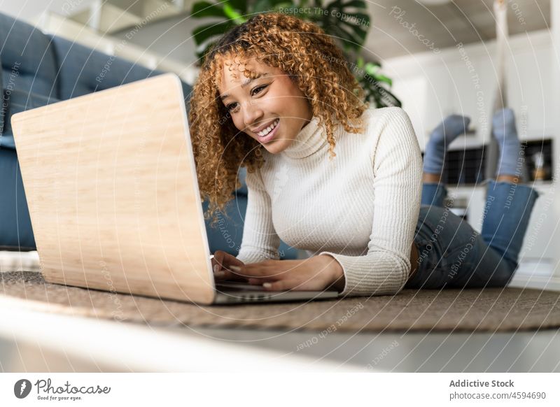Cheerful black woman using laptop at home typing smile independent delight freelance floor work lying female ethnic lady cheerful gadget browsing carpet