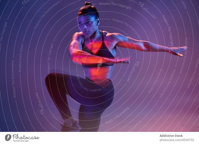 Strong woman doing exercise in studio sportswoman training wellness neon fit energy workout purple sportswear young athlete slim illuminate dark practice