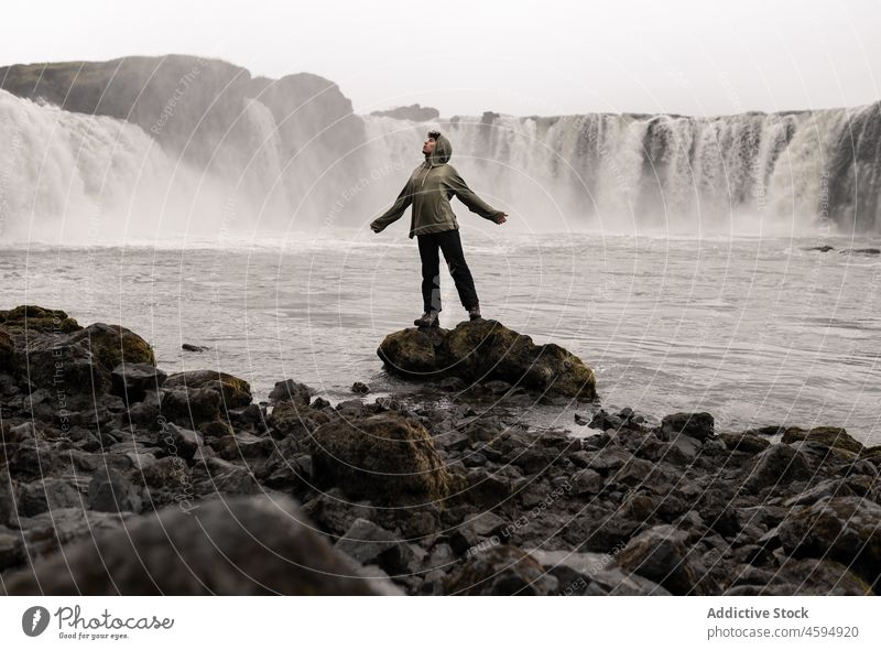 Tourist outstretching arms while standing on stone near foamy waterfall man explore freedom nature wanderlust cascade harmony rock adventure male highland