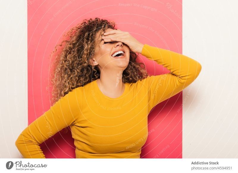 Young woman laughing and covering eyes with hands curly hair bright young colorful style happy cheerful trendy joy casual positive vibrant hand on head smile