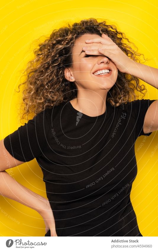 Young woman laughing and covering eyes with hands curly hair bright young colorful style happy cheerful trendy joy casual positive vibrant hand on head smile