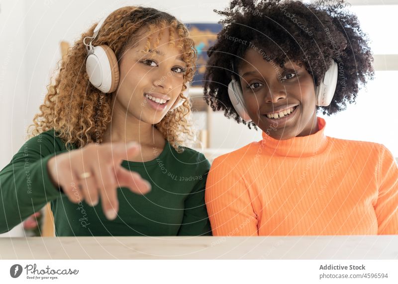 Cheerful diverse women with headphones showing saluting gesture friend positive greeting vlog afro social media hello happy smile together curly hair vlogger