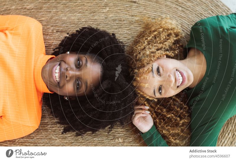 Positive multiethnic women friends lying on carpet together floor smile happy friendship relax carefree positive weekend bonding comfort rest leisure home