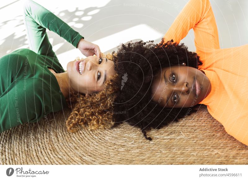 Positive multiethnic women friends lying on carpet together floor smile happy friendship relax carefree positive weekend bonding comfort rest leisure home