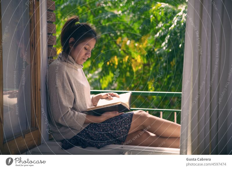 Girl reading a book in the frame of her window. Reading Reader Book Window Window frame Education Literature Study Colour photo Novel