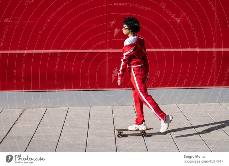 African American woman with short hair and red sportswear riding on her skateboard with red background female Spain clothes wall standing curly hair beauty