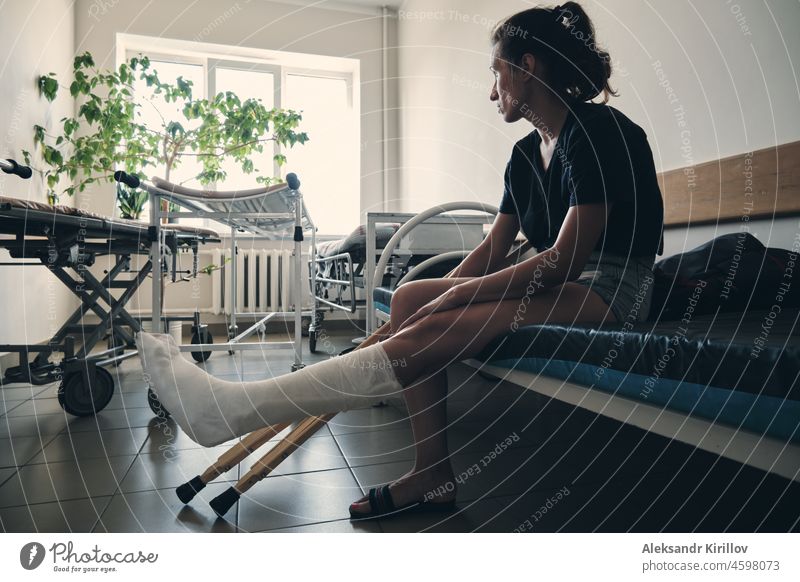 A woman with a broken leg sits on a hospital couch and looks out the window. Leg injury. Loss of mobility. Rehabilitation after a fracture person sitting ankle