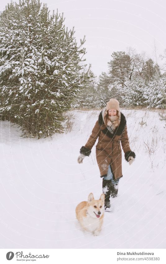 Happy woman running with her corgi dog on a walk in the snowy forest in winter candid moment lifestyle white female fun caucasian active person pet walking