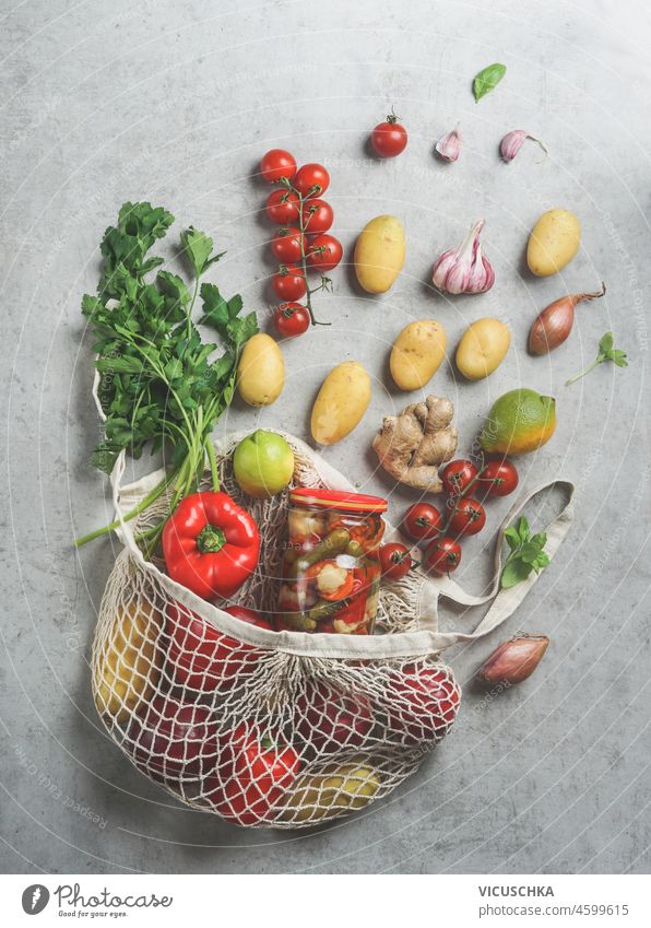 Sustainable groceries shopping bag with various vegetables: potatoes, tomatoes, pepper, lime, herbs, garlic, onion and preserve on grey concrete table. Plastic free lifestyle . Top view. Zero waste