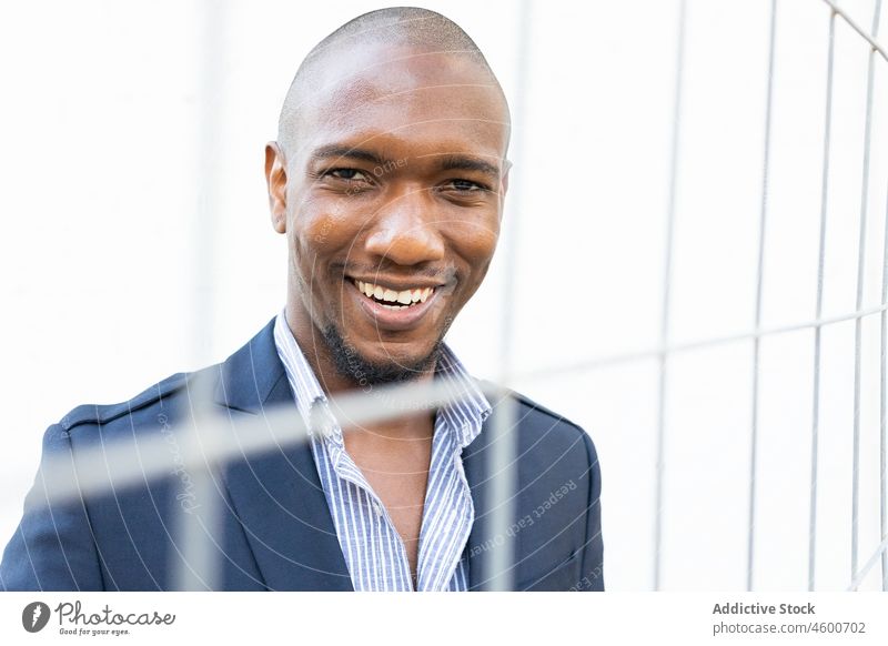 happy black man behind metal fence formal net trapped imprisoned predicament smile captive problem trouble appearance street cheerful city male african american