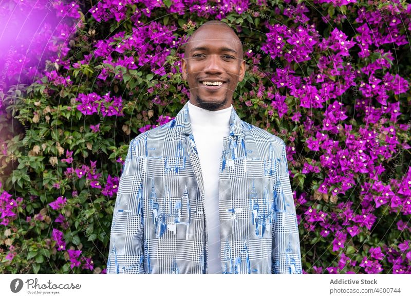 Cheerful black man near blooming bush style fashion street plant park flower floral male african american positive glad optimist happy smile beard bald guy town