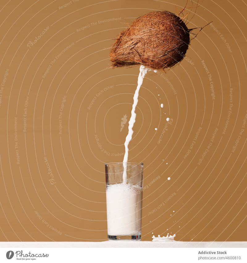 Coconut milk pouring into glass in brown studio coconut delicious healthy beverage exotic tropical fresh sweet vitamin nutrition motion splash fill serve drink