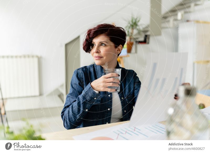 Woman with water glass examining graphs woman diagram chart freelance analyze work workplace project document data thirst home analysis paper occupation desk
