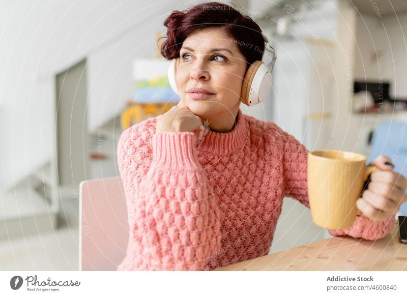Woman with tablet drinking beverage and listening to music in headphones woman hot drink cup refreshment thoughtful modern device gadget using home optimist