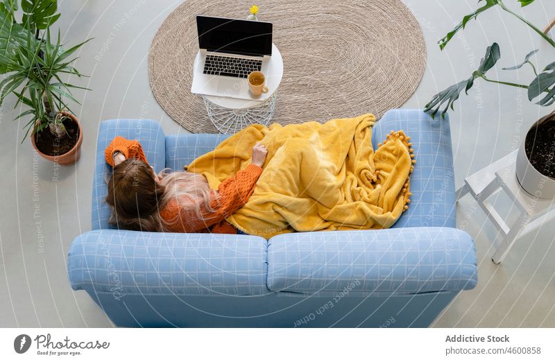 Anonymous woman on couch watching video on laptop cozy comfort internet weekend free time leisure rest movie plaid sofa device netbook female browsing gadget