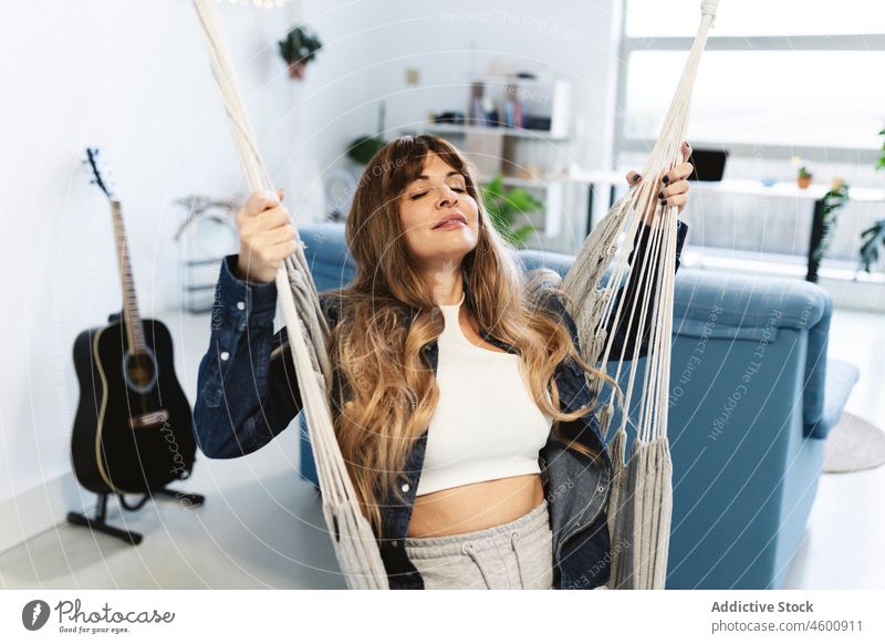 Relaxed woman resting in hammock relax living room domestic chill pastime swing recreation eyes closed guitar acoustic apartment home sofa comfort casual