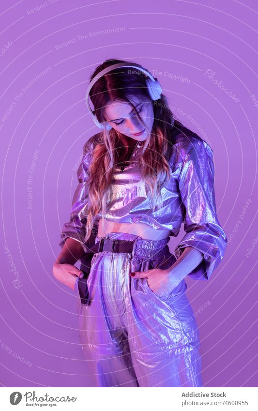 Futuristic female in stylish outfit standing in studio with neon illumination woman illuminate listen style futuristic thoughtful headphones 80s personality